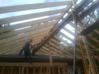 Rafters going up over a new addition with a worker on the wall in Byron